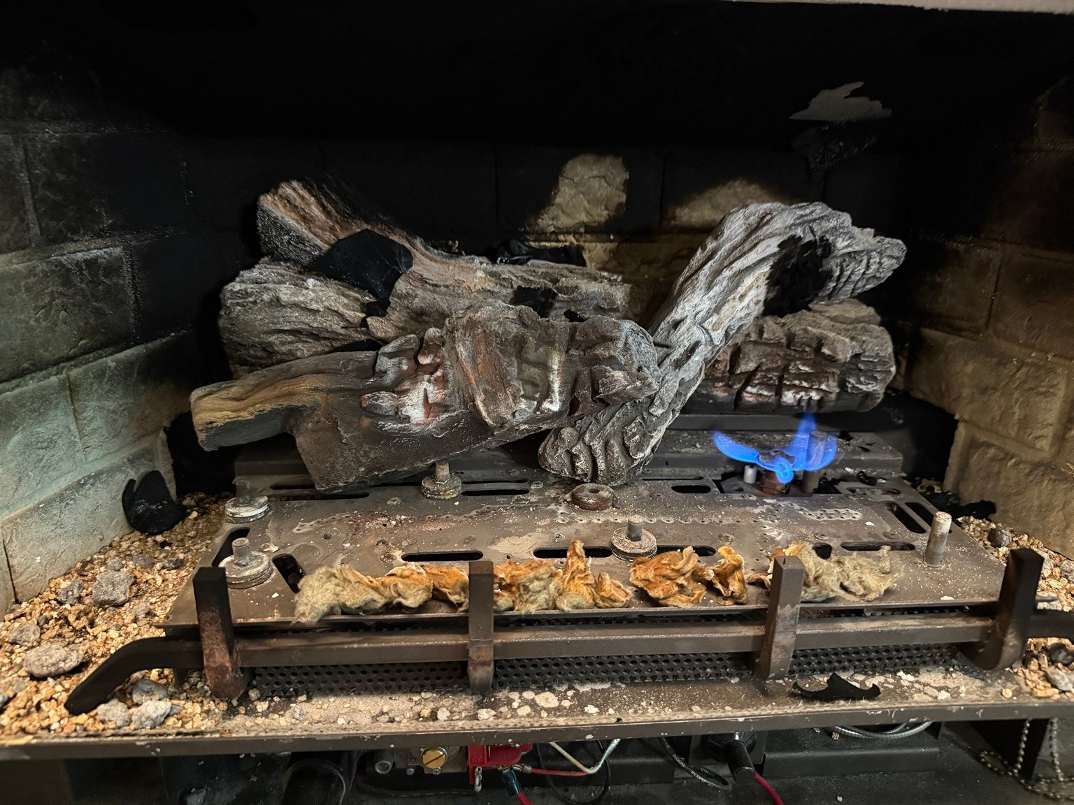 Close-up inside a gas fireplace showing logs, burner components and a blue flame