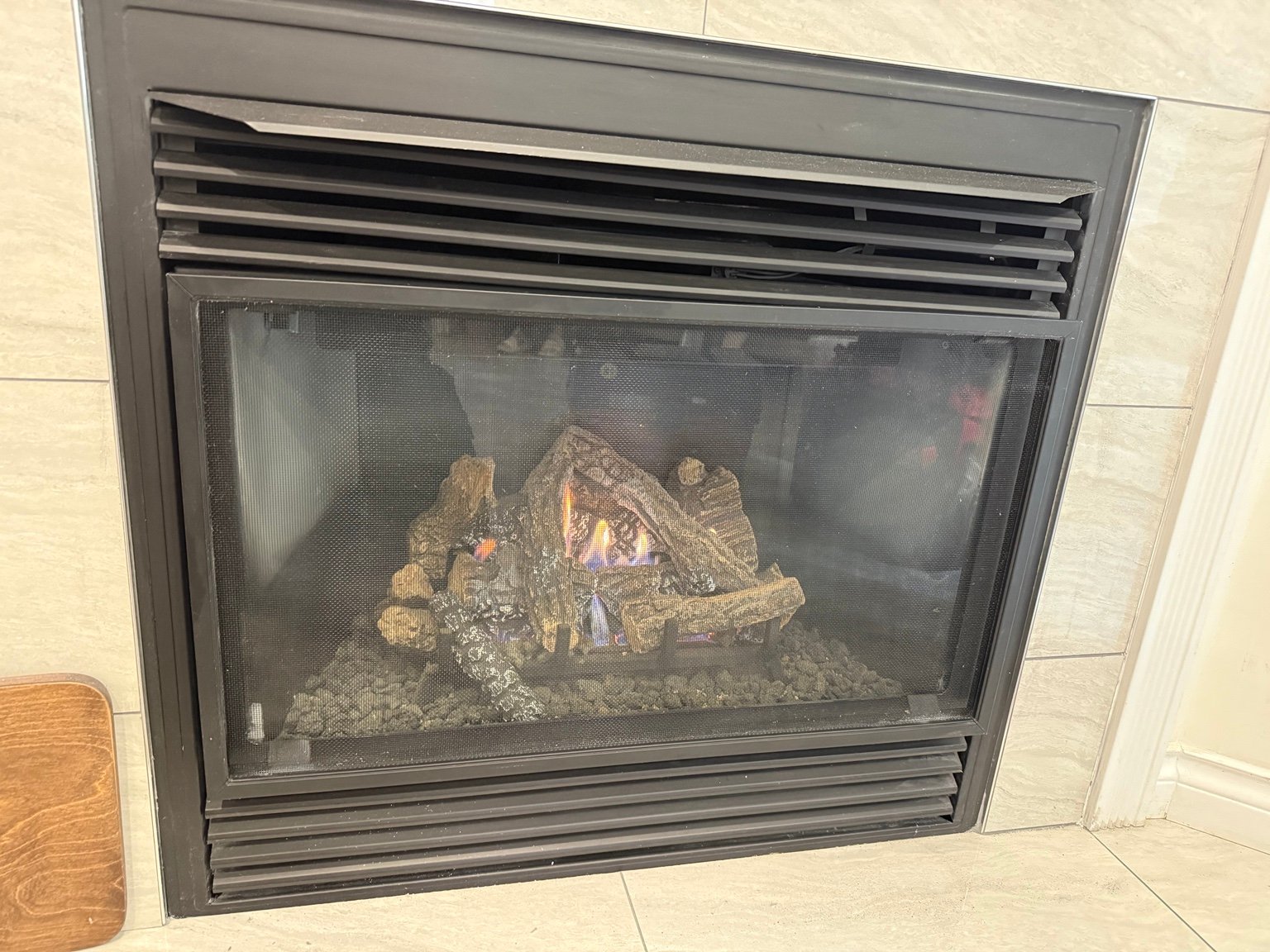 Lit gas fireplace behind a protective screen with black trim and tile surround