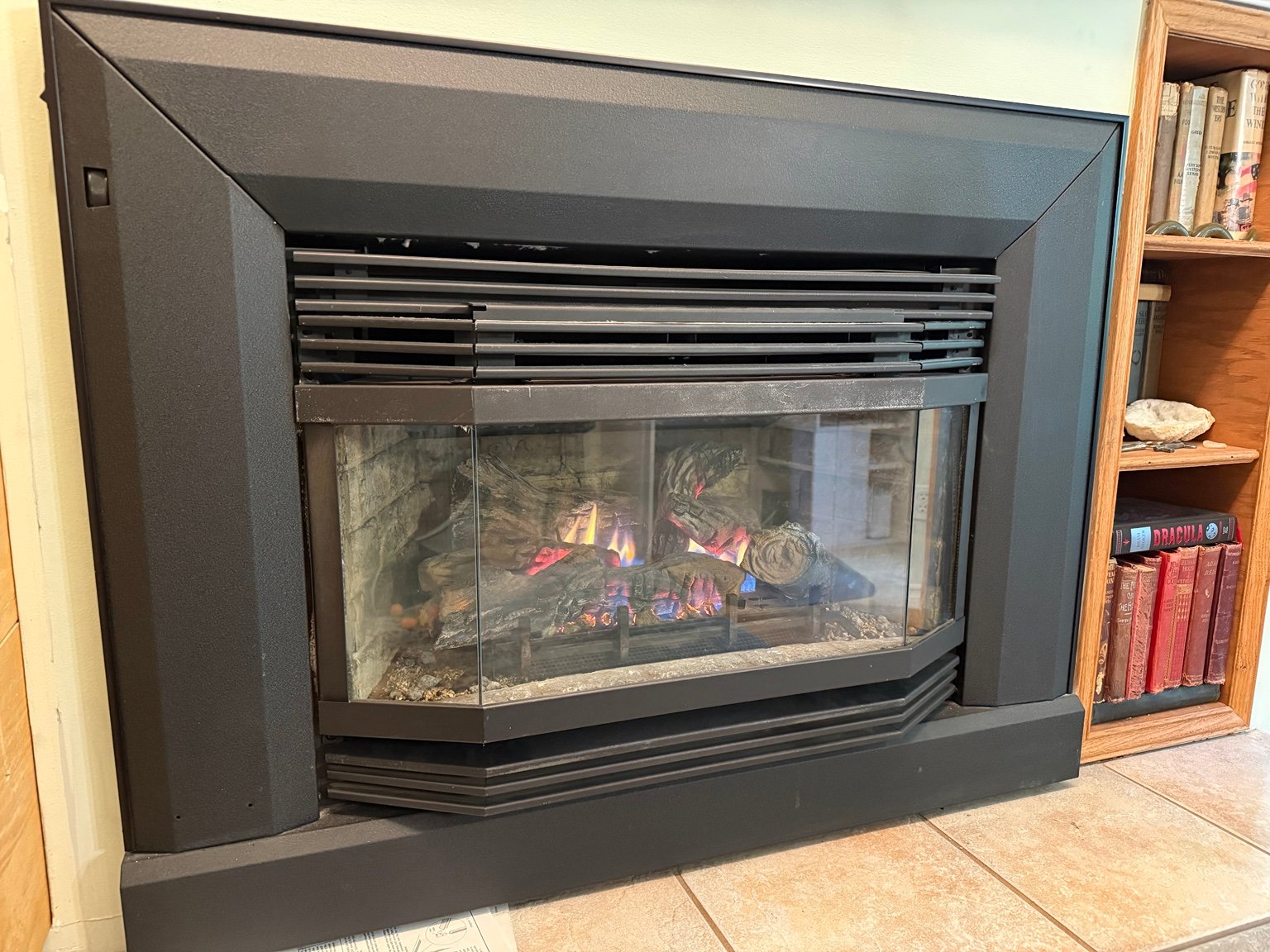 Lit gas fireplace with black surround and glass front beside a wooden bookshelf